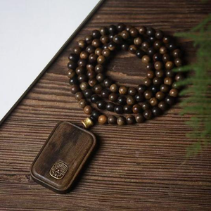 Agarwood amulet pendant with dark bead necklace and gold-tone emblem on brown case